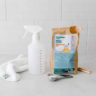 Frasco pulverizador branco, saco de percarbonato de sódio, colher com pó, pano branco e superfície clara