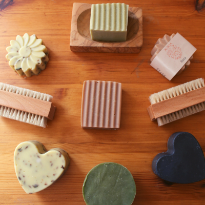 Sabões artesanais em várias formas e cores com escovas de cerdas naturais sobre madeira