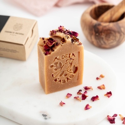 Sabonete bege com pétalas de rosa secas sobre base de mármore branco.