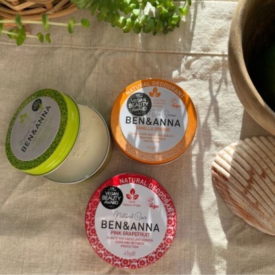 Três latas redondas de desodorantes naturais BEN & ANNA em cores verde, laranja e vermelha sobre tecido bege