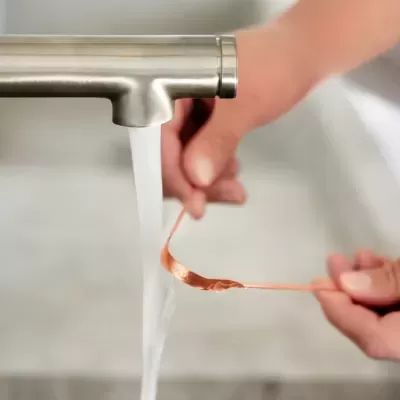 Torneira metálica moderna com água a correr e mãos a segurar fio de cobre