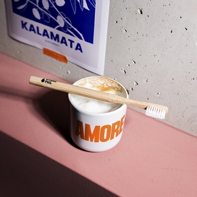 Escova de dentes de madeira sobre chávena com bebida e arte azul na parede.