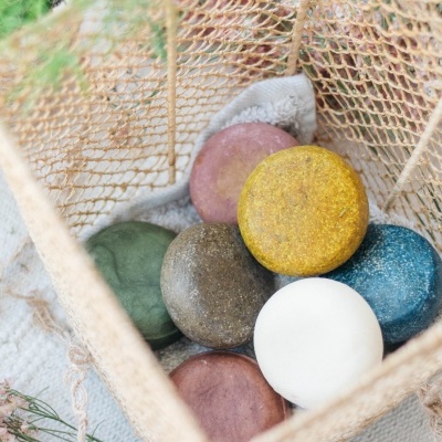 Sabonetes coloridos em cesto de malha rústica sobre tecido claro