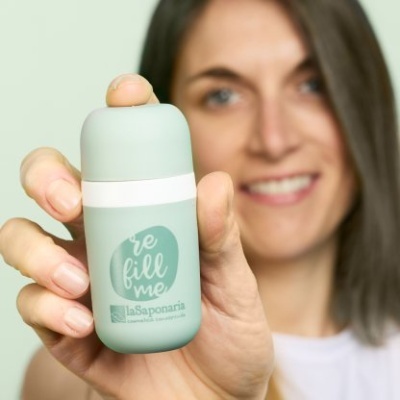 Frasco verde com tampa branca e etiqueta 're fill me' segurado por mulher