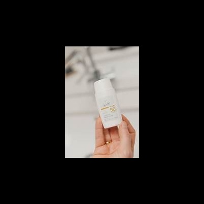 Frasco de protetor solar branco com rótulo amarelo e cinza, mão segurando, fundo desfocado