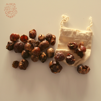 Frutos secos e saco de pano cru com cordões sobre superfície clara e logotipo ALDEIA SABÃO