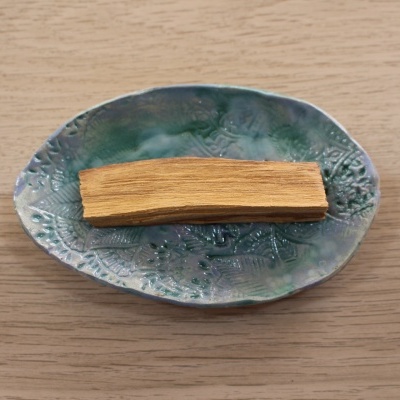 Prato oval de cerâmica azul esverdeada com padrão floral e pedaço de pau de madeira clara