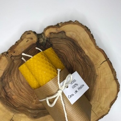 Vela amarela de cera de abelha enrolada em papel castanho com etiqueta e laço, sobre pedaço de madeira rústica.