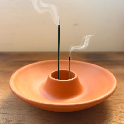 Suporte de incenso circular em cerâmica terracota com incensos acesos e fumaça
