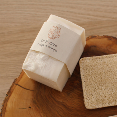 Sabão artesanal em papel reciclável ao lado de esponja em madeira