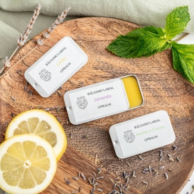 Três latas pequenas de velas perfumadas em base de madeira com limões e folhas verdes