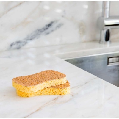 Dois esfregões amarelos com lado abrasivo castanho claro sobre bancada branca em mármore ao lado de pia