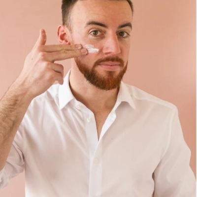 Homem a aplicar creme facial no rosto com fundo cor de pêssego