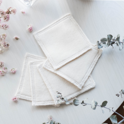 Toalhitas quadradas brancas em tecido macio com bordas costuradas sobre mesa branca com flores secas