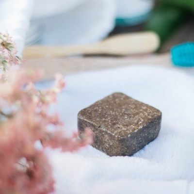 Bloco quadrado castanho na toalha branca com escova ao fundo e flores rosas