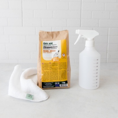 Pacote de ácido cítrico com rótulo amarelo, frasco spray plástico transparente e pano branco