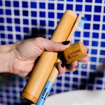 Mão a segurar estojo, escova de dentes de bambu e tampa com texto Hydro Phil