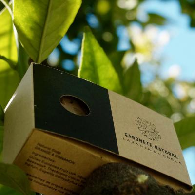 Sabonete natural com embalagem de cartão dourada e preta ao ar livre junto a folhas verdes