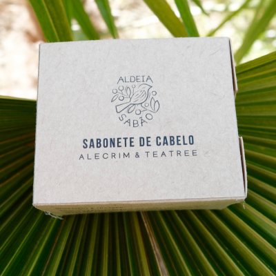 Caixa de sabonete de cabelo Alecrim & Teatree da Aldeia Sabão sobre uma folha verde