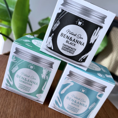 Caixas de pasta de dentes Ben&Anna nos modelos Black, Sensitive e White sobre mesa de madeira com planta ao fundo