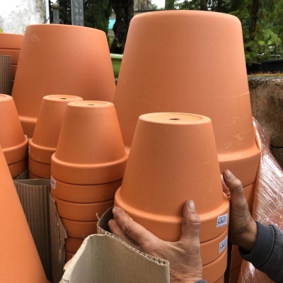 Vasos de barro empilhados em tons terracota com mãos a segurar um vaso