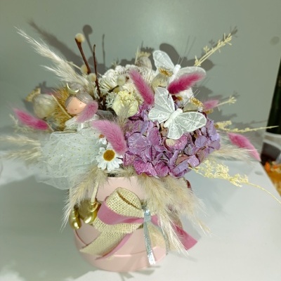 Arranjo floral artificial com flores roxas e brancas em vaso rosa e laço decorativo