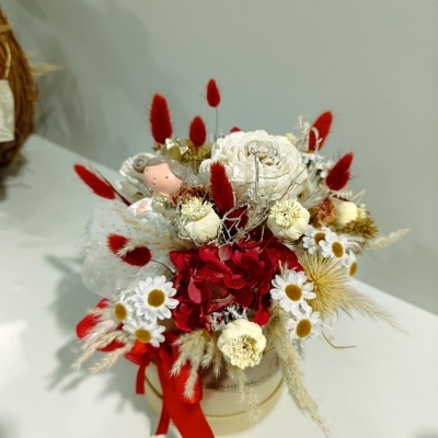 Arranjo floral colorido em vaso redondo creme com fita vermelha e pequeno boneco decorativo