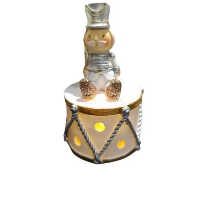 Figura decorativa de soldadinho branco e dourado sentado em tambor iluminado