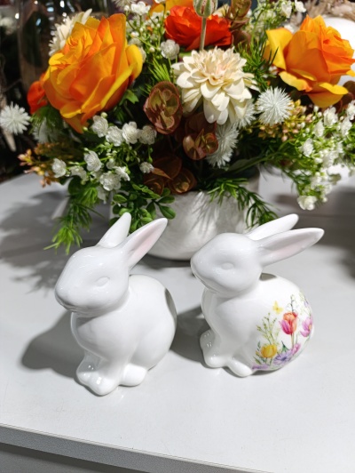 Dois coelhos de cerâmica branca decorativos com flores ao fundo