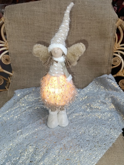 Anjo decorativo de tecido com saia luminosa, chapéu e asas sobre tecido brilhante