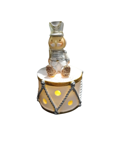 Figura decorativa de soldadinho branco e dourado sentado em tambor iluminado