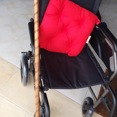 Cadeira de rodas preta com almofada vermelha e bengala de madeira