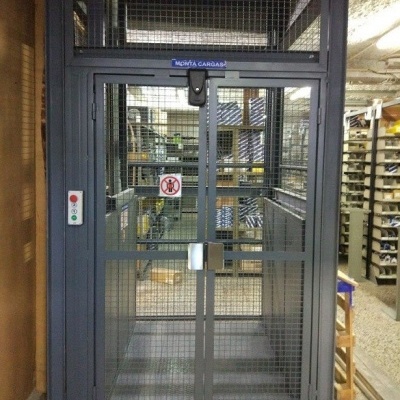 Elevador de carga metálico cinzento com portas de rede em armazém
