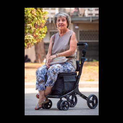 Mulher idosa sentada numa cadeira de rodas preta com bolsa frontal em ambiente urbano