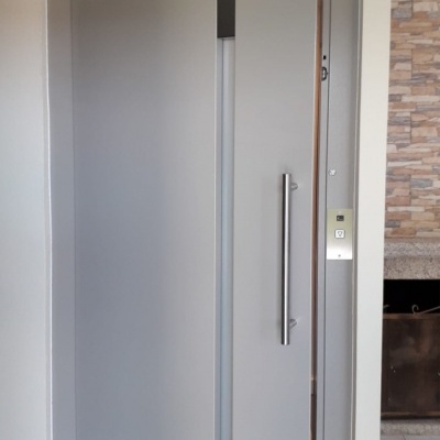 Porta pivotante cinza claro com puxador metálico instalada em interior moderno.