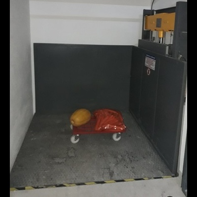 Plataforma elevatória industrial com carrinho e objetos no interior