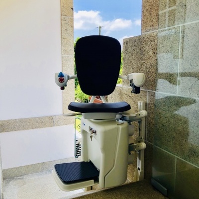 Cadeira elevatória preta e branca instalada num patamar entre paredes de pedra e vidro