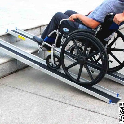 Pessoa em cadeira de rodas preta a subir rampa portátil metálica cinzenta com ajuda de outra pessoa