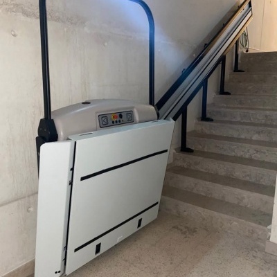 Plataforma elevatória branca e preta com painel de controlo e escadas de pedra ao lado