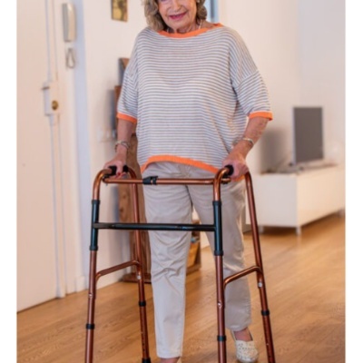 Idosa com andador metálico cor de cobre dentro de casa