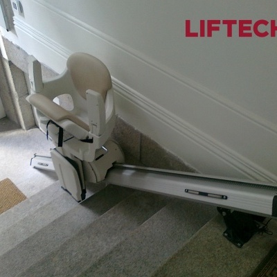 Cadeira elevatória branca marca LIFTECH instalada em escadas interiores cinzentas com texto Move up.