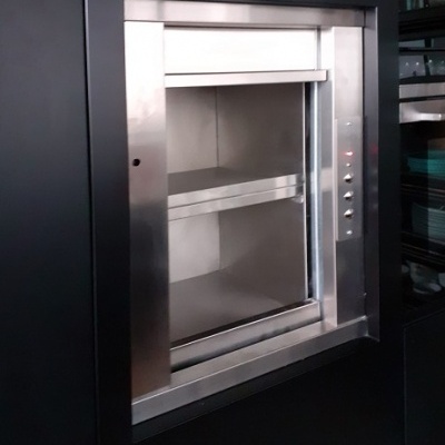 Elevador de alimentos em inox com portas de vidro embutido numa parede preta