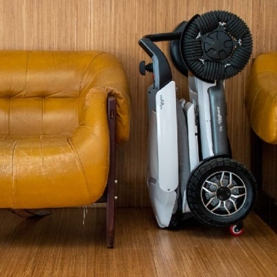 Scooter elétrica dobrável branca e preta entre poltronas de couro amarelo e parede de madeira