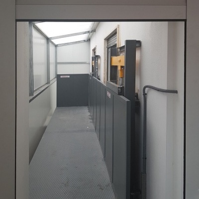 Plataforma elevatória para acessibilidade com estrutura metálica cinza e cobertura transparente