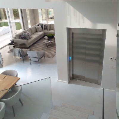 Elevador metálico doméstico em ambiente interior branco moderno com escadas e sala de estar