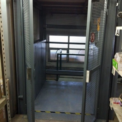 Elevador de carga industrial com portas metálicas em rede e piso antiderrapante em armazém