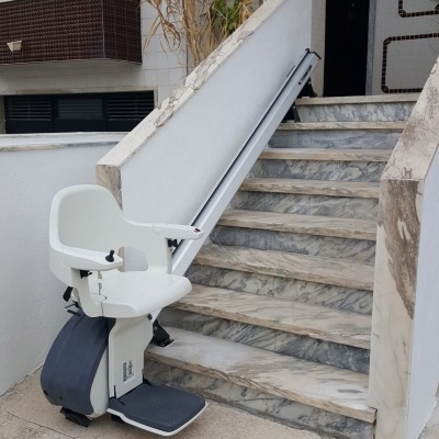 Cadeira elevatória branca para escadas com degraus em mármore e marca LIFTECH no chão