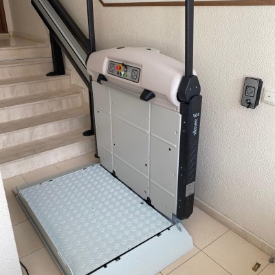 Plataforma elevatória acessível instalada ao lado de escada interior com controles na plataforma e autocolante LIFTECH Move up