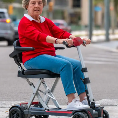 Scooter elétrico de mobilidade cinza com assento preto e guiador vermelho numa calçada urbana