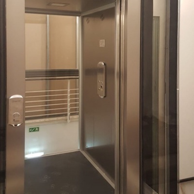 Elevador residencial metálico prateado com portas automáticas de vidro e interior escuro